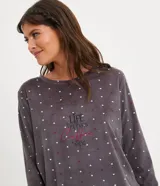 Pijama largo de plush gris con estampado de lunares blancos y corazones rojos. Incluye una blusa de manga larga con cuello redondo y un pantalón con puños ajustados.