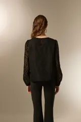 Blusa negra de poliéster con diseño texturizado de ondas, cuello redondo a la base y mangas largas transparentes con puños elásticos.