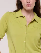 Camisa blanca de manga corta con cuello solapa, cierre frontal de botones, detalles bordados al tono en el pecho y lazos para anudar en las mangas.