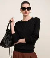 Blusa de manga larga negra confeccionada en punto de viscosa con poliamida e hilos metálicos, con cuello redondo y hombreras. Presenta textura de rayas curvas que forman rombos.