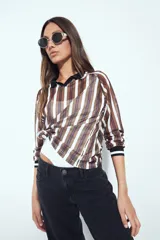 Remera de manga larga con tejido tipo mesh, diseño de rayas verticales en tonos marrones y blancos, cuello polo negro y puños tejidos con detalle de rayas.