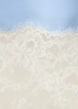 Vestido corto de tejido satinado color celeste, con diseño recto, escote recto y tirantes finos. Presenta detalles de encaje blanco en el escote y en el ruedo.