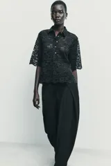 Camisa de encaje negro con cuello solapa, manga corta y cierre frontal con botones.