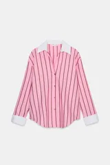 Camisa oversize de popelina rosa con rayas verticales marrones, cuello solapa blanco y escote en pico. Mangas largas con puños anchos blancos a contraste y cierre frontal con botones.
