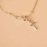 Pulsera tipo denario confeccionada en plata 925, compuesta por una cadena fina con pequeñas esferas intercaladas y un dije colgante en forma de cruz.