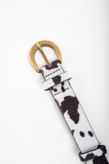Cinto de cuero sintético con estampado de vaca en blanco y negro, hebilla metálica dorada y forro interior negro.