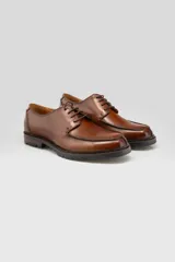 Zapato acordonado de cuero color marrón, diseño tipo derby con costuras marcadas en el empeine y suela gruesa track de goma.