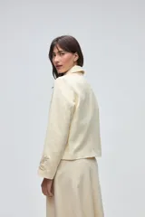 Chaqueta de lana fina sin teñir, con cuello clásico y bolsillos frontales. Presenta detalles bordados en el cuello y en los puños de las mangas. Es una prenda forrada con diseño exclusivo.