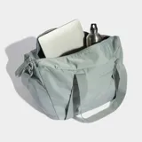 Bolso deportivo Adidas de diseño minimalista en color gris, con correas de hombro integradas y correa ajustable extraíble. Cuenta con un bolsillo frontal con cierre y logo de la marca estampado en tono sobre tono.