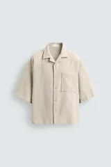 Camisa de corte boxy fit confeccionada en tejido con mezcla de lino. Presenta cuello bowling, manga corta, bolsillo plastrón en el pecho y cierre frontal con botones.