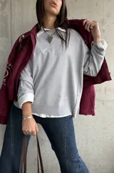 Sweater de punto color gris, de corte holgado y diseño de manga larga con costuras visibles en los hombros. Presenta cuello redondo y puños acanalados.