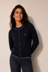 Cardigan de punto color azul marino, con cierre frontal de botones, escote redondo y detalles de ribetes en color celeste y naranja. Presenta un delicado bordado en el pecho y diseño de mangas largas.