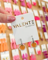 Aros colgantes plateados con dije circular color naranja con borde de strass. El aro mide 1,5cm de diámetro y el dije 1,5cm de diámetro. El material del aro es acero.