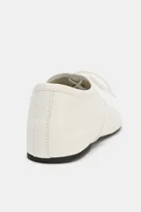 Zapatos planos de piel color blanco, con cierre de cordones en el empeine y detalle de pespuntes decorativos.