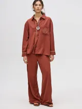 Pantalón de corte holgado y tiro alto con caída recta, color azul petróleo. Presenta una franja lateral decorativa en tonos rojo y amarillo que recorre la pierna, a juego con la camisa de la misma línea.