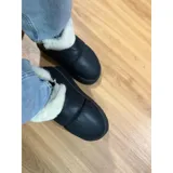 Pantuflas botitas color tostado con diseño acolchado y plataforma, forradas con corderito sintético blanco en el interior y el cuello. Cuentan con una pequeña etiqueta decorativa en el lateral.