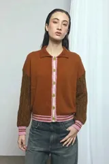 Cardigan de punto color marrón, con cuello vuelto, cierre frontal de botones y detalles de ribetes a rayas en los puños, la cintura y la botonera. Las mangas presentan un diseño tejido en relieve con textura de ochos.