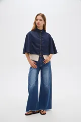 Poncho corto de denim azul con cuello alto, cierre frontal y diseño amplio de inspiración capa.