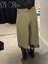 Bermuda de corte sastrero color beige, con diseño de pierna ancha y largo midi. Presenta detalle de encaje negro en el ruedo y bolsillos traseros simulados.