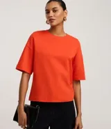 Blusa básica de mujer color negro, confeccionada en malla encorpada de algodón, con cuello redondo y mangas cortas de corte oversized con sisas desplazadas.
