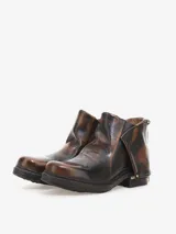 Bota corta de cuero bovino negro con efecto desgastado y envejecido, con detalles en gris claro. Presenta un diseño con solapa frontal que se ajusta con un broche y una cremallera lateral expuesta en el talón. Posee un taco bajo y cuadrado.