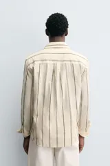 Camisa de corte relajado confeccionada en tejido mezcla de algodón, con diseño de rayas verticales, cuello solapa, manga larga con puños abotonados y cierre frontal de botones.