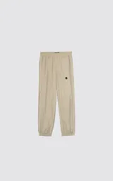 Pantalón deportivo de microfibra color beige, con corte regular y diseño de inspiración vintage. Presenta vivos laterales a contratono, cintura elástica y puños elásticos en los tobillos.