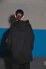 Buzo negro oversize de frisa con capucha amplia, bolsillo canguro, terminaciones de puño y ruedo con rib, y logo bordado en el centro delantero.