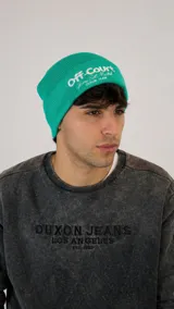 Gorro tipo beanie de punto acanalado en color verde, con bordado frontal en color blanco que incluye texto y detalles gráficos.