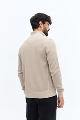 Campera de algodón color beige, estilo deportivo con cierre frontal, cuello alto y puños. Presenta bolsillos laterales y un pequeño logo bordado en el pecho.