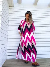 Vestido camisero largo con diseño de estampado chevron en colores fucsia, beige y negro. Presenta cuello camisero, cierre frontal con botones y mangas tres cuartos.