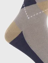 Media de caña media con diseño de rombos en tonos beige, gris y azul marino. Presenta un pequeño bordado del logo de la marca en uno de los rombos.