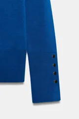 Jersey Zara de punto liso color negro, con cuello redondo, manga larga y detalle de botones dorados en los puños.