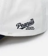 Gorra blanca de sarga con visera azul marino y bordado de Snoopy jugando baseball.