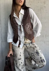 Chaleco de gamuza color chocolate con bordados decorativos en color crudo y cierre frontal con cordones y borlas.