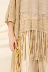 Poncho artesanal color beige con hilos de lurex dorados y terminación de flecos. Diseño irregular, más corto adelante que atrás.