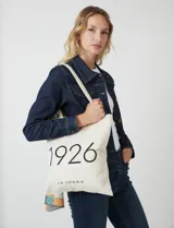 Tote bag de tela color crudo con estampado tipográfico negro en el frente que dice 1926 y La Opera. Cuenta con asas largas para llevar al hombro.
