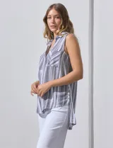 Camisa sin mangas de corte recto, con cuello clásico y escote en V. Presenta un diseño de rayas verticales en tonos lila, rosa, blanco y gris, con dos bolsillos frontales aplicados con estampado en chevron. Cuenta con cierre central de botones.