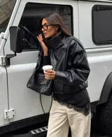 Chaqueta de cuero sintético color negro con acabado granulado, diseño oversize, cuello alto estructurado y cierre asimétrico.