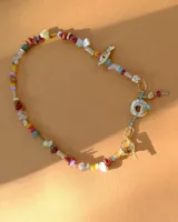 Collar corto de estilo artesanal, compuesto por una variedad de piedras naturales en tonos tierra, verdes, rojos y amarillos, intercaladas con pequeñas perlas de río. Presenta dijes de bronce macizo con formas orgánicas, incluyendo una figura de pez y un dije circular central, unidos por un cierre de barra y argolla.