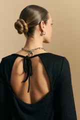 Top negro de manga larga acampanada con escote pronunciado en la espalda que se ajusta con lazos. La tela presenta una textura sutil con brillo, similar a un animal print discreto.