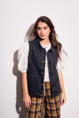 Chaleco oversize de denim negro con costuras en hilo ocre, cuello camisero, cierre frontal con botones y bolsillos delanteros.