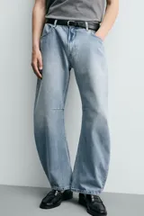 Jeans de denim de algodón en color negro con efecto lavado, corte amplio y silueta curva tipo barrel fit con pinzas en las rodillas. Presenta diseño clásico de cinco bolsillos y cierre frontal con cremallera y botón metálico.