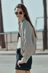 Chaqueta estilo bomber con estampado de cuadros vichy en blanco y negro, de cuello subido, manga larga y bolsillos delanteros de vivo. Cuenta con bajo abullonado y cierre frontal con cremallera oculta.