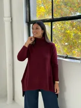 Sweater de punto color bordó con cuello alto tipo polera, diseño de corte evasé con costura central vertical y bajo asimétrico más largo en la parte posterior.