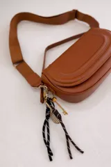 Cartera bandolera de tamaño compacto en color camel, con diseño estructurado y solapa frontal. Incluye doble asa: una corta fija de cuero sintético y una correa larga estilo sport regulable. Cuenta con cierre de cremallera y broche imantado, además de un detalle de llavero colgante.