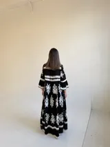Vestido largo negro con estampado floral blanco, escote en V con cuello mao, cierre frontal de botones y mangas tres cuartos acampanadas.