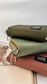 Billetera corta de diseño capitoneado con cierre perimetral y solapa frontal. Cuenta con compartimentos internos para tarjetas y billetes, e incluye una correa de mano desmontable.