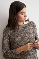 Sweater de punto con textura jaspeada en tonos marrones, de corte recto, cuello redondo y mangas largas. Presenta un diseño con ruedo curvo.
