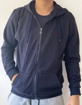 Campera de algodón azul marino sin felpa, con capucha ajustable mediante cordones, cierre frontal completo y bolsillos tipo canguro. Presenta un pequeño bordado rojo en el pecho.